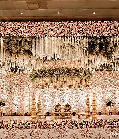 A spectacular, wall-to-wall floral stage we created for a grand Indian wedding reception. The backdrop features a dense arrangement of white and pink flowers with hanging tuberose strings, showcasing our capability for large-scale floral installations.