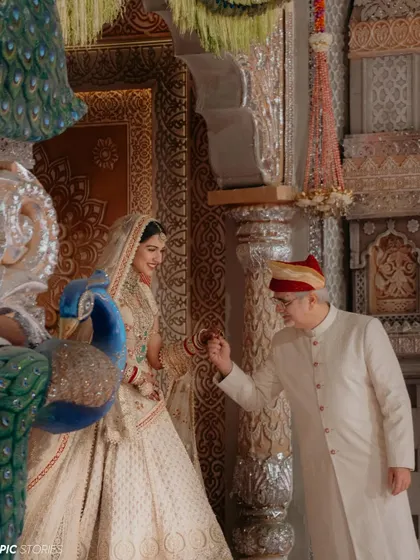 A beautiful, candid moment between Radhika and her father. The gentle interaction and shared smile amidst the grandeur of the temple setting highlight the deep, personal connections that are at the heart of every wedding.
