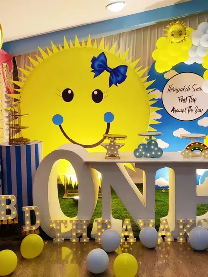 A bright and cheerful "First Trip Around the Sun" themed birthday. The setup features a giant smiling sun backdrop, a 'ONE' marquee table, and a blue and yellow color scheme.