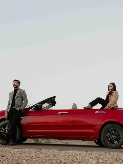 A stylish shot of a couple with a red convertible on a desert road, exuding a cool, road-trip romance vibe.