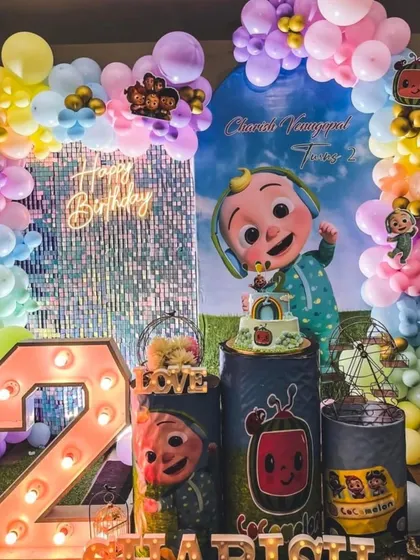 A grand Cocomelon party for Charish's second birthday, this setup includes a shimmering sequin wall, a large light-up number '2', and plenty of colorful balloons and characters.