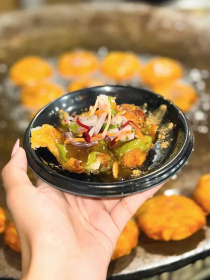 A freshly prepared plate of Nawabi Tikki chaat, held up against the backdrop of more tikkis sizzling on the tawa. This is street food at its finest, served fresh and hot.