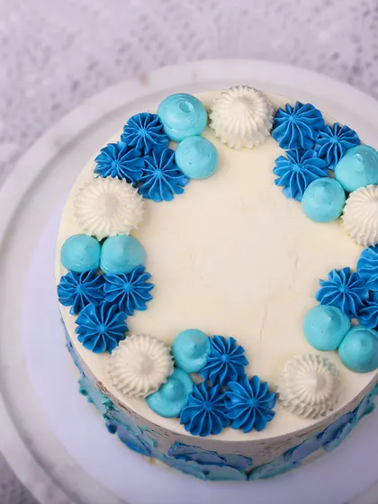 We create a piece of modern art with this abstract blue buttercream cake. Strokes of various blue shades are painted onto a white canvas, accented with gold splatters and topped with piped rosettes, making it a stylish and happy choice for a Father's Day celebration.
