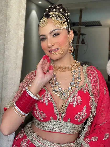 A happy bride showing off her complete red lehenga look. The combination of the outfit, jewellery, and traditional red alta on her hands creates a timeless bridal image.