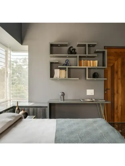 In the Shivom residence, this bedroom combines a cool grey palette with a warm wooden door. The custom geometric shelving unit serves as both storage and a wall feature.