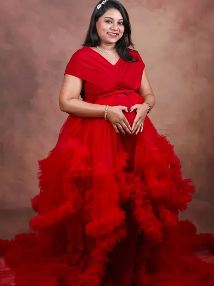 A happy client making a heart shape over her bump in a vibrant red ruffled gown. This studio shot showcases the dress's incredible volume and rich color.