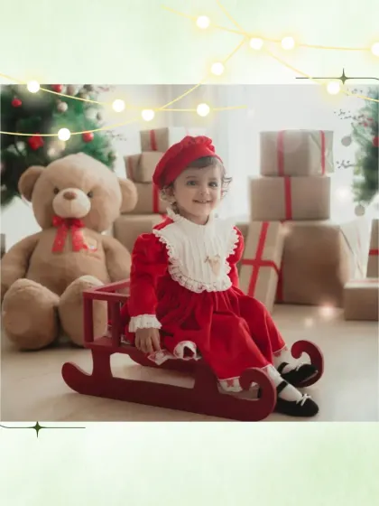 Ready for a sleigh ride. This little girl is picture-perfect in her red Christmas dress, sitting by the presents under the tree.