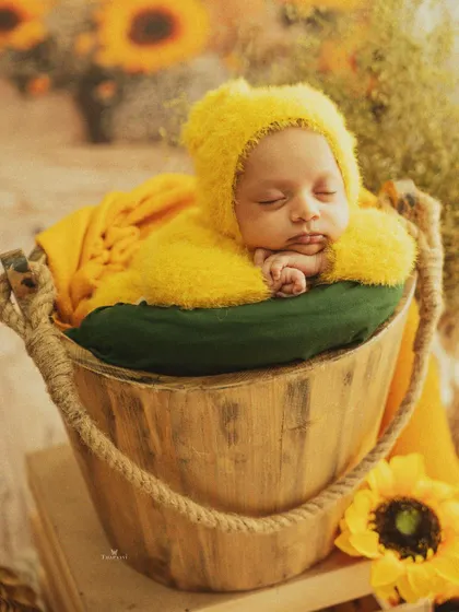 A bucket full of sunshine. This newborn, dressed in a fuzzy yellow outfit, sleeps soundly in a rustic wooden bucket surrounded by bright sunflowers.