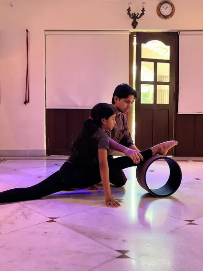 In a private coaching session, I'm guiding a student through a split stretch using a yoga wheel. This prop helps to safely deepen the stretch and improve alignment for young gymnasts and dancers.