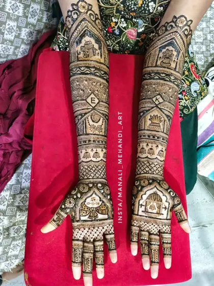 A full-arm bridal design featuring temple gopuram architecture at the top. The arms are filled with various bands of geometric patterns and a personalized initial 'E' for the bride.