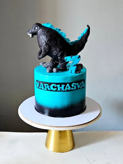 A fearsome Godzilla cake for a 7th birthday. The cake features a black and turquoise airbrushed finish and is topped with a powerful, hand-sculpted, and fully edible Godzilla figurine.