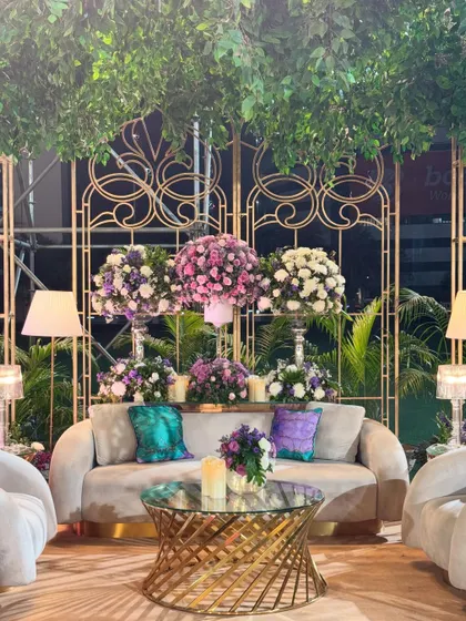 Spelling comfort and luxury with these gorgeous seating corners. Nestled under a canopy of lush greens and accented with purple florals, these spaces are both elegant and inviting.