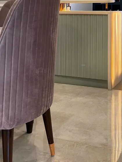 This image highlights the beautiful glow of the backlit Onyx bar counter, seen from behind a plush velvet dining chair. The light reflects off the polished floor, adding to the room's luxurious ambiance.