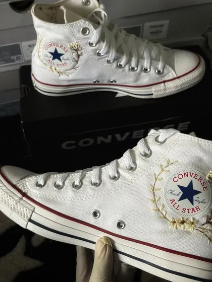 The embroidered Converse held up, showcasing the detailed threadwork.