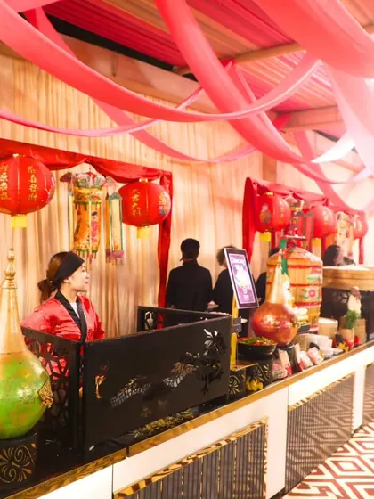 A Chinese-themed buffet station with red lanterns and other decorative elements, set against a backdrop of pink and cream drapery. We tailor our presentation to match your event's theme perfectly.
