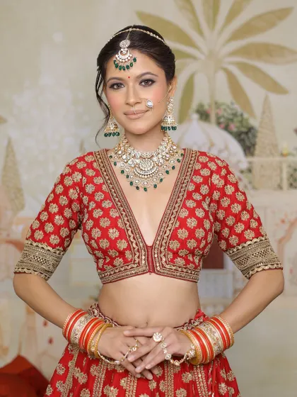 A full portrait of a stunning bride in her red lehenga. The makeup is designed to enhance her features, with a focus on glowing skin and expressive eyes, making her look and feel like royalty.