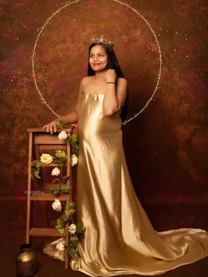 A regal portrait of a mom-to-be in a shimmering golden gown, complete with a crown and a halo of light. This setup creates a divine, goddess-like image celebrating motherhood.