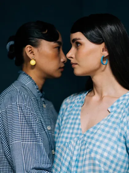 An intimate nose-to-nose portrait for Label Rama. The shot highlights the models' profiles and the contrast between their gingham shirts and colorful earrings.