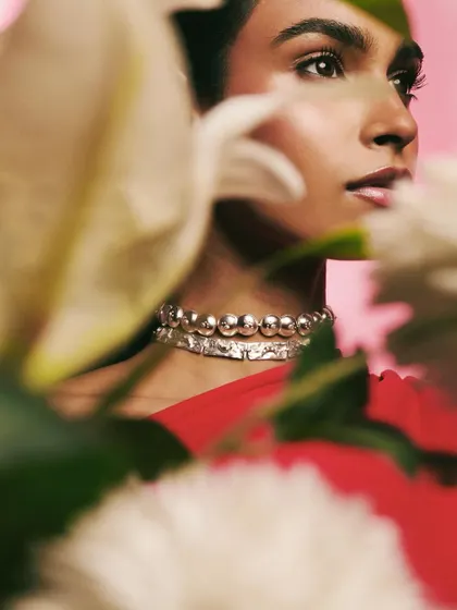 An intimate, through-the-flowers view of the model wearing a silver choker for Batoki.art. This creative framing adds depth and a sense of discovery to the jewelry photograph.