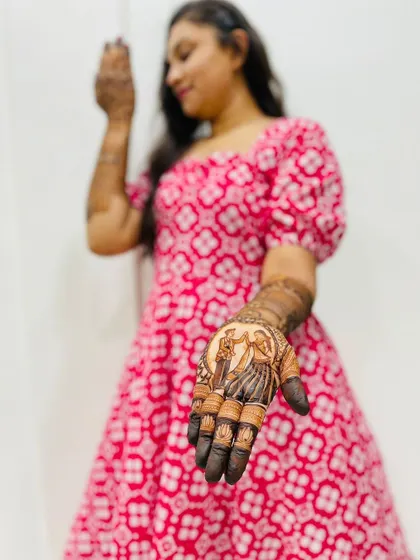 A bride showcasing her custom mehndi, which features a portrait of the couple on her palm.