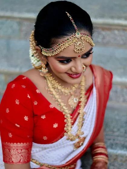 A smiling close-up of the bride, highlighting her intricate gold temple jewelry, including the maang tikka and necklaces.