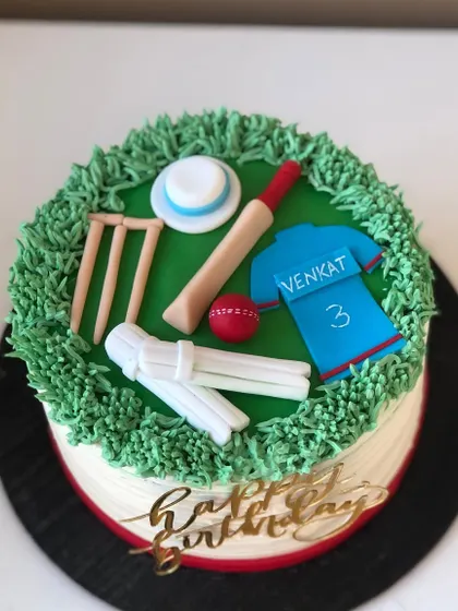 A cricket-themed cake with a pitch made of buttercream grass, complete with a bat, ball, wickets, and a jersey.