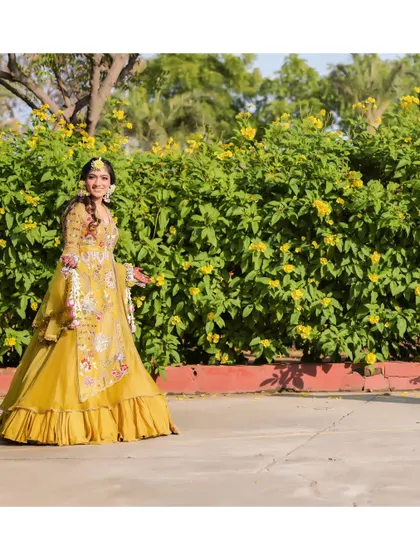 The bride enjoying a quiet moment during her outdoor Haldi ceremony in Jaipur. Her yellow embroidered lehenga and floral jewelry stand out beautifully against the natural greenery.