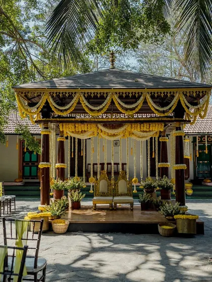A classic Haldi ceremony mandap decorated entirely in shades of yellow and white. The traditional structure is adorned with marigold garlands and hanging floral strings, creating a bright and auspicious setting.