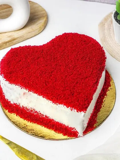 An elegant composition of a heart-shaped red velvet cake with golden cutlery.
