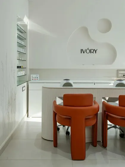 'The Ivory' nail salon by Studio Mudh features a clean, minimalist design with a custom-designed reception desk and bold orange chairs.