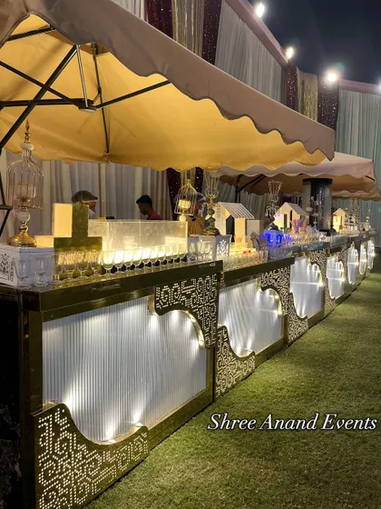 This is one of my charming outdoor beverage counters, set up under a canopy. The illuminated white and gold design features cute miniature house displays for juices, creating a whimsical and inviting look.