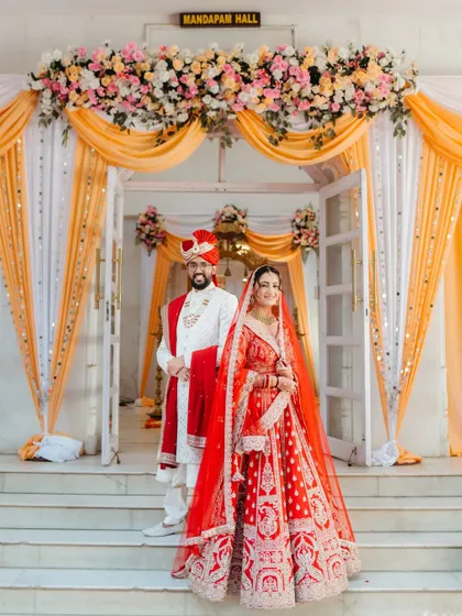 A classic portrait of the bride and groom, perfectly framed by the floral decor of their wedding hall. This is a timeless shot that captures the elegance and grandeur of the wedding day.
