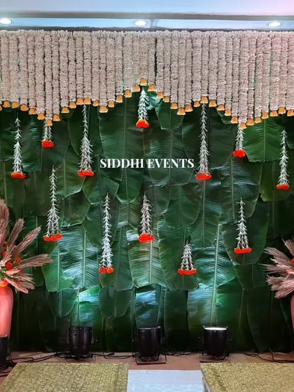 We love blending natural elements with traditional florals. This unique stage backdrop features a wall of fresh green banana leaves, beautifully contrasted with hanging curtains of white and red tuberose, offering a touch of South Indian elegance to the celebration.