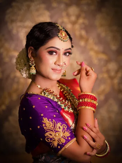 A close up portrait that captures the essence of a traditional bride. The makeup is subtle yet defining, with a focus on the eyes and a lip color that complements the purple and red saree.