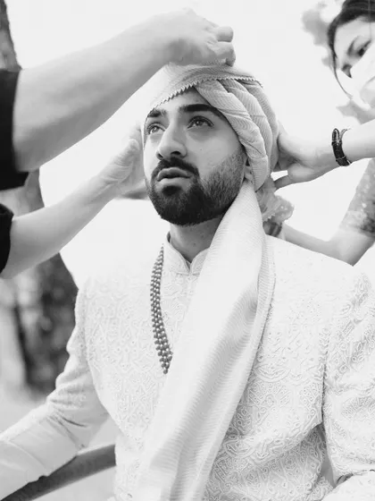 A powerful black and white shot of the groom getting his turban tied. This getting-ready moment is captured with an editorial eye, focusing on tradition and anticipation.