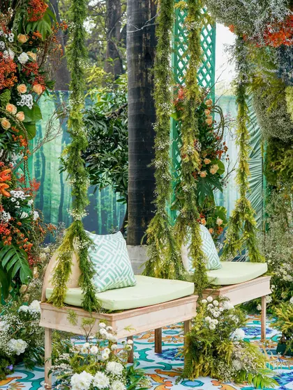 A wider view of the moss-draped floral swing, showing how it is nestled within a lush, green, forest-like environment.