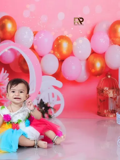 A full view of the pink-themed cake smash setup, with the birthday girl happily sitting next to her cake. The "One" sign and decorative birdcages add a whimsical touch.
