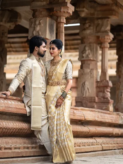 A classic and romantic portrait of the couple in their traditional wedding attire, posing against the ancient stone pillars of a temple.