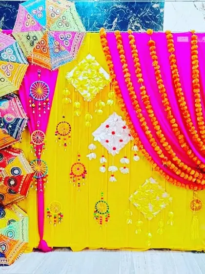 A bright and cheerful Mehendi backdrop with yellow and pink drapes, decorated with marigold strings and colorful umbrellas.