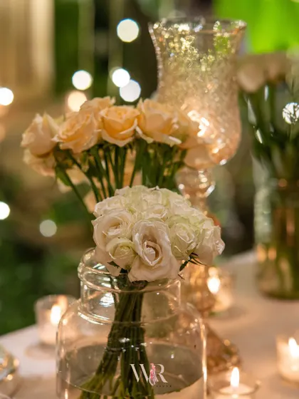 A close-up of simple, elegant floral arrangements in glass jars, surrounded by the soft bokeh of fairy lights. This detail shot captures the magical and romantic quality of the lighting design.