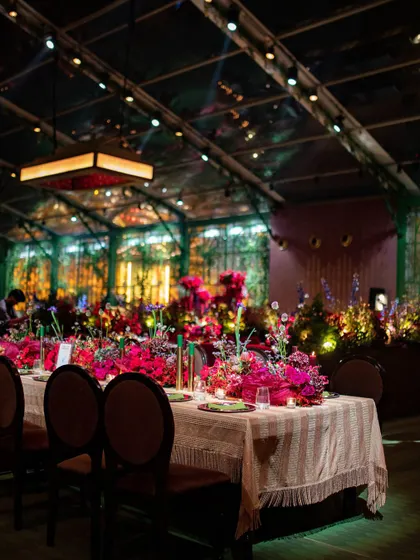 A long dining table covered in vibrant pink florals, set under a clear-span tent for an elegant dinner experience during the Sangeet.