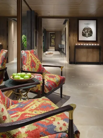 The entrance to the Caitriona apartment, where 'Arizona Armchairs' upholstered in a hand-woven durrie create a welcoming vignette. The space is a blend of rich textures, from the Sukupira wood veneer to the Burberry Beige stone floor.
