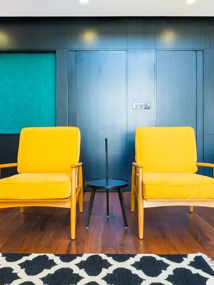 A detail shot of the modernist living room, focusing on the two mustard-yellow chairs. The dark wood wall with teal alcoves behind them creates a rich, high-contrast backdrop that is both bold and sophisticated.