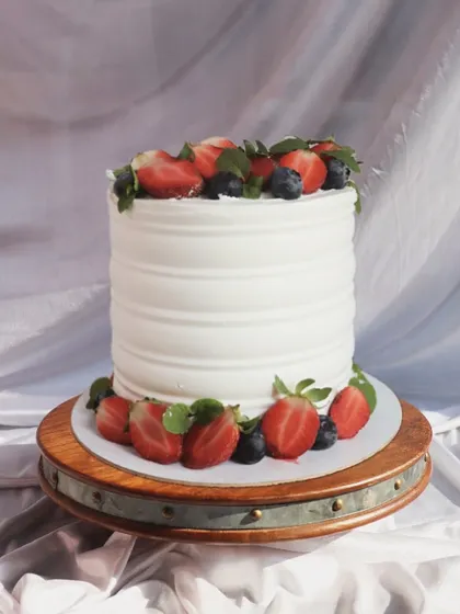 A simple white cake with a ribbed texture, beautifully decorated with fresh strawberries and blueberries around the top and bottom.