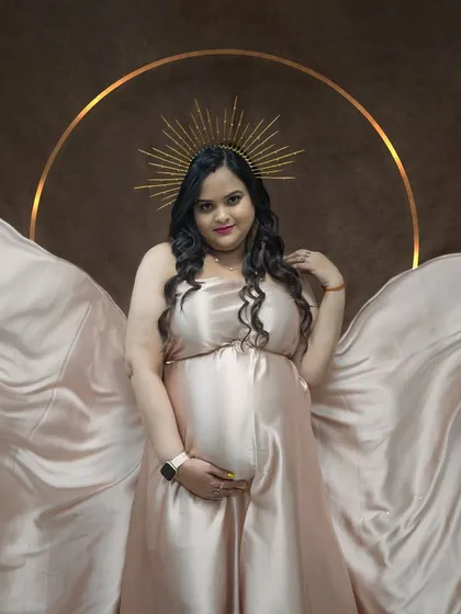 Another look at the champagne satin gown. Here, we've draped the fabric around the mom-to-be to create a soft, angelic look, complemented by the halo prop.