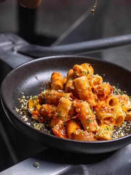 A beautiful bowl of Rigatoni pasta, ready to be served. The rich sauce clings to every piece, and a final drizzle of oil gives it a beautiful sheen.