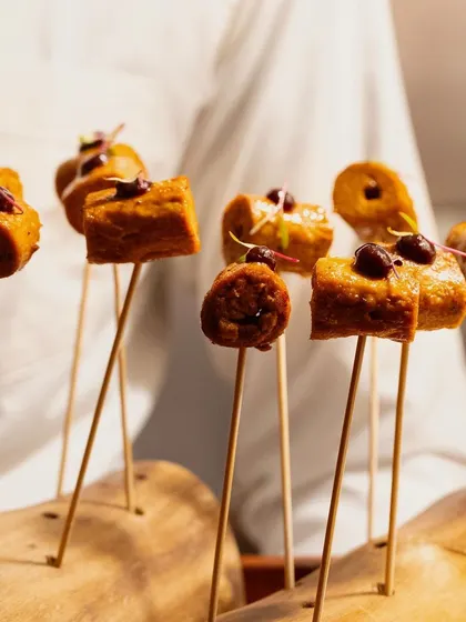 A chef presents a wooden platter of our savory kebab skewers, a highlight from our Modern Indian canapé selection.