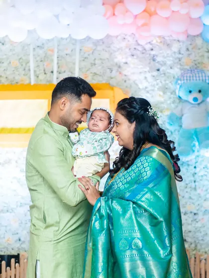 A beautiful portrait from a naming ceremony. The parents, dressed in soft pastel traditional wear, gaze lovingly at their newborn baby, creating a serene and heartwarming image.