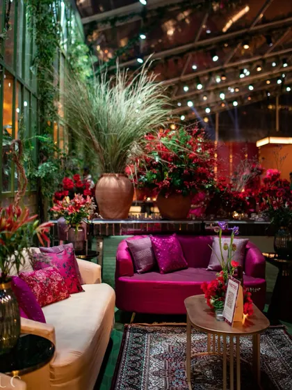 A cozy lounge area with plush sofas in jewel tones, set against a greenhouse-style glass wall, offering a space for guests to relax and mingle.