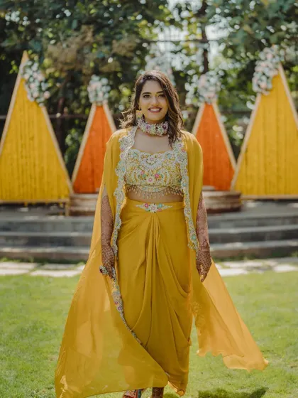 The bride poses in front of the colorful triangular Haldi backdrop, showcasing her festive attire.